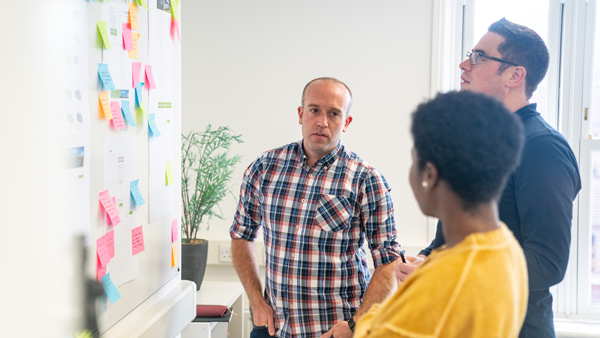 Experience UX Team, Ali, Matt and Jestine have a discussion in front of a whiteboard