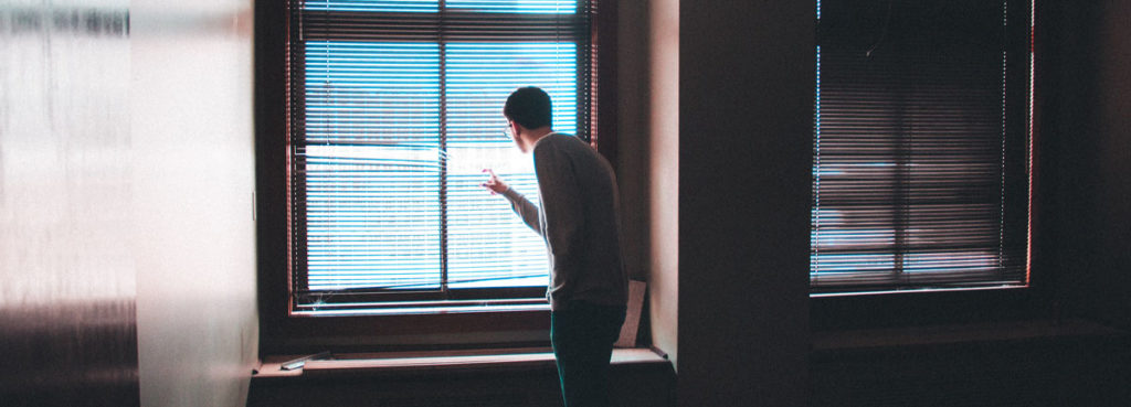 a person inside a room looking through the shutter of a window