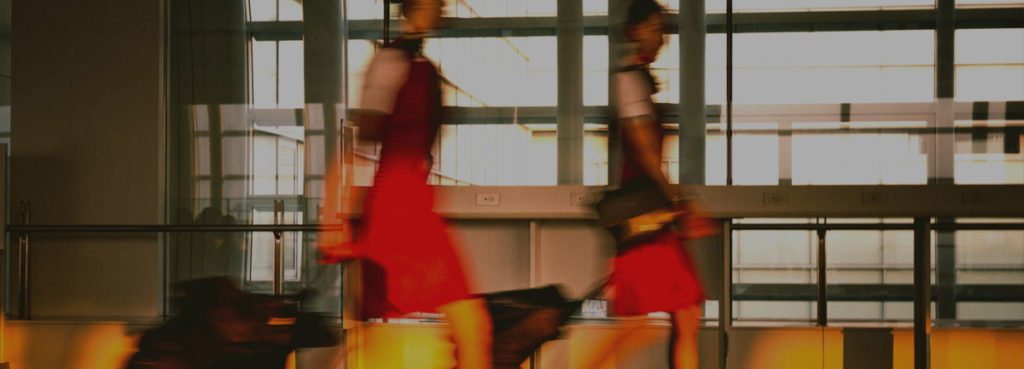 Image of two people pulling along suitcases in what could be an airport. The image is slightly blurred to give the impression of movement.