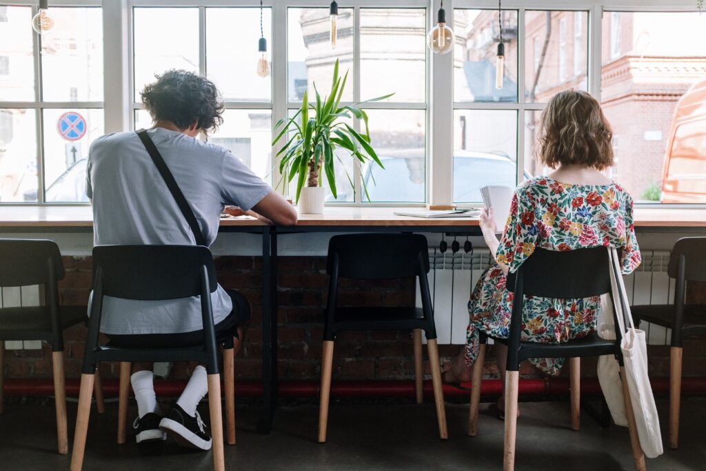 Two people, sitting on chairs at a window table, with their backs to camera.